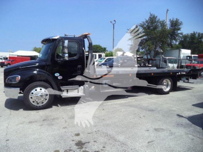 Freightliner M2 106 Plus rollback truck in a dealership lot showing cab and flatbed.