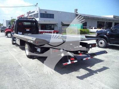 Freightliner M2 106 Plus rollback truck with flatbed and tow setup, viewed from rear-left in parking lot.