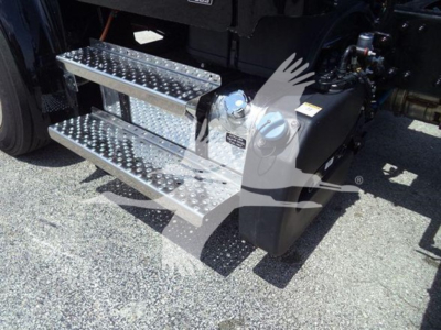 Step/run-flat steel steps with diamond tread beside Freightliner M2 106 Plus cab; fuel filler cap visible; hydraulic reservoir area; part of chassis and drivetrain.