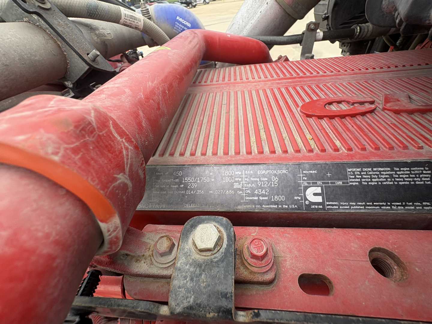 Peterbilt engine bay showing label plate with specifications and red air intake hose and metal clamps.