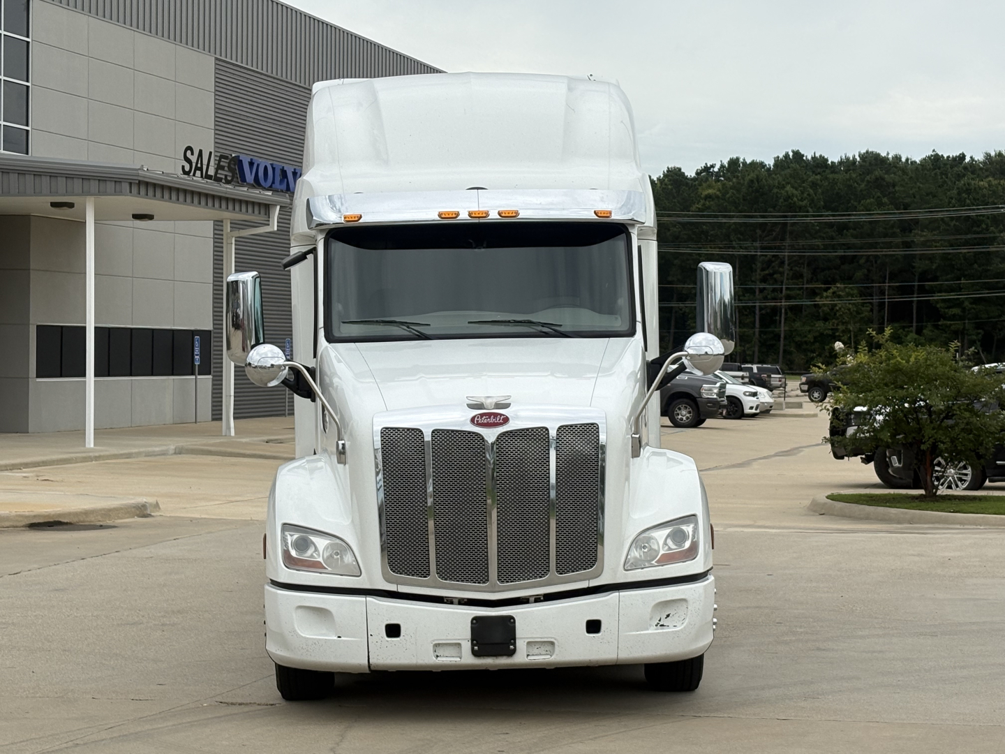 Peterbilt 579 truck front view in a dealership lot, white cab with chrome grille, tall sleeper, and side mirrors visible.