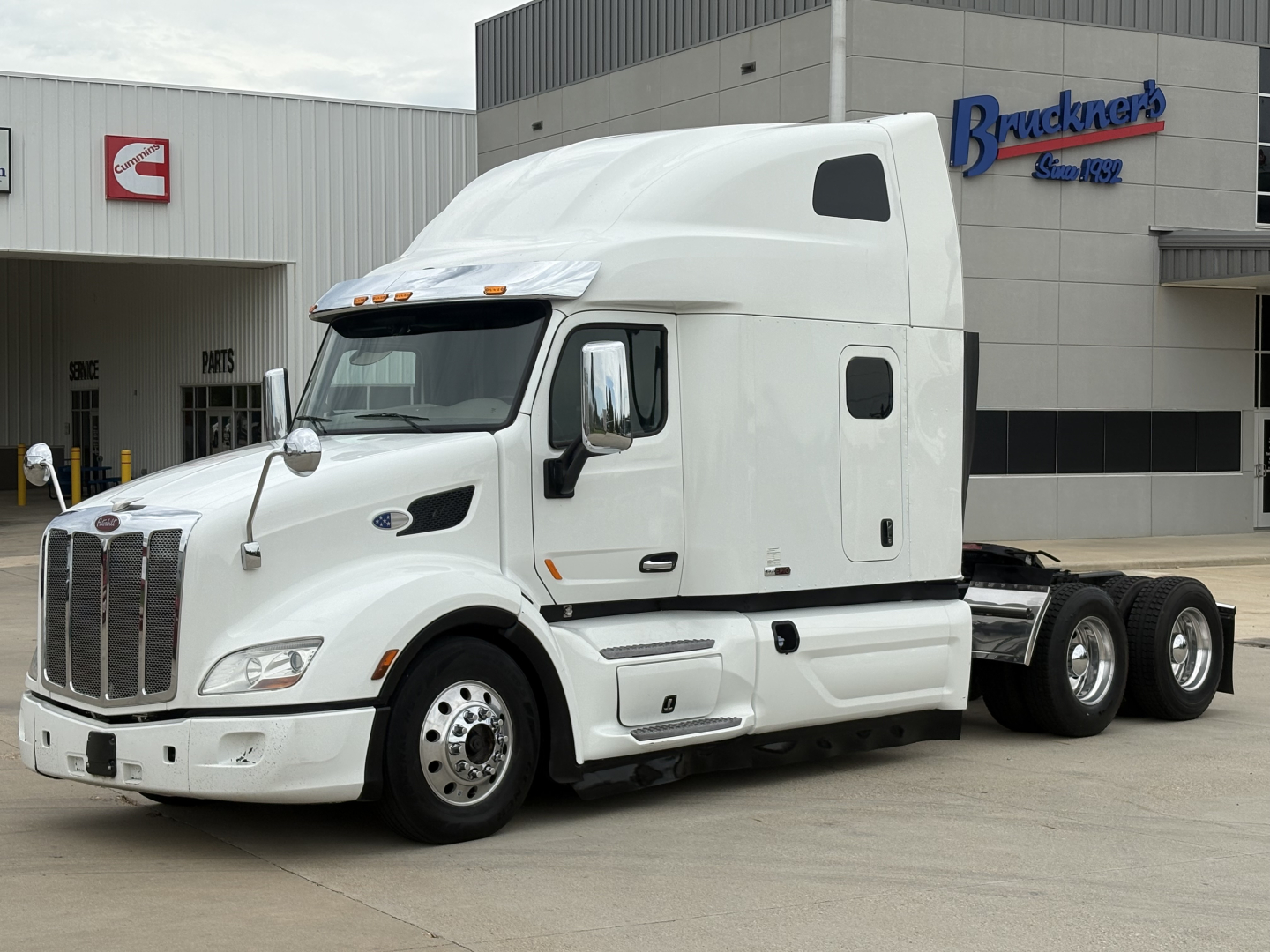 Peterbilt 579 sleeper cab tractor in white, side view with tractors, year 2020, showing cab and dual rear axles, front grille and wheels.