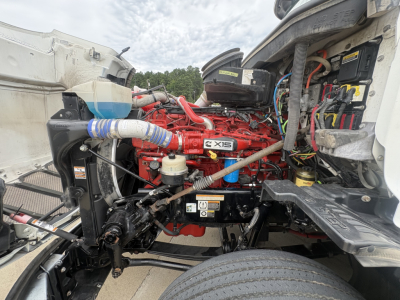 Peterbilt 579 engine bay showing Cummins X15 engine with red color, surrounding hoses, belts, and label stickers.