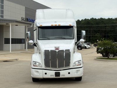 Peterbilt 579 truck front view in a dealership lot, white cab with chrome grille, tall sleeper, and side mirrors visible.
