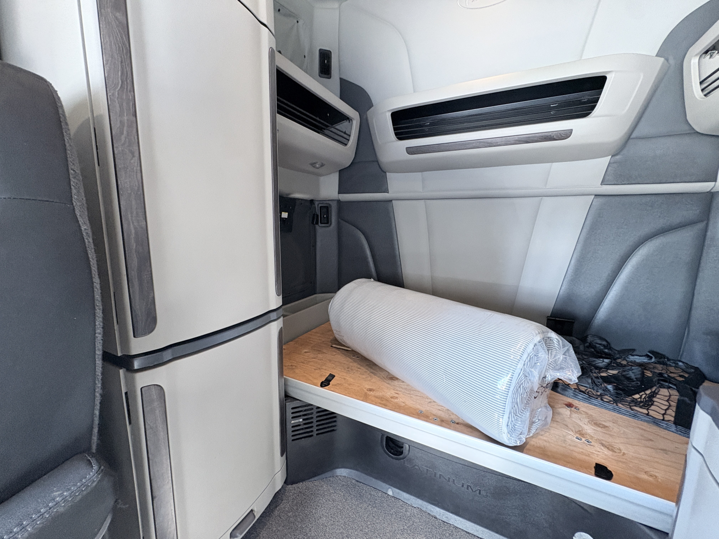 Peterbilt 579 cab interior showing sleeper area with rolled mat on wooden shelf and overhead side panels.