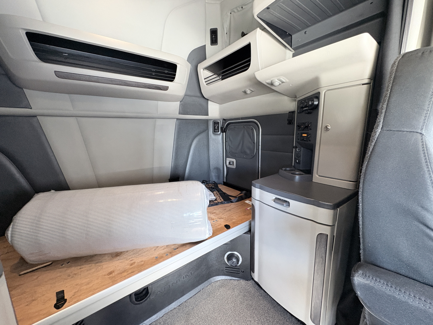 Peterbilt 579 sleeper cab interior showing side bed with mattress and storage cabinet, dashboard controls, and overhead storage panels.