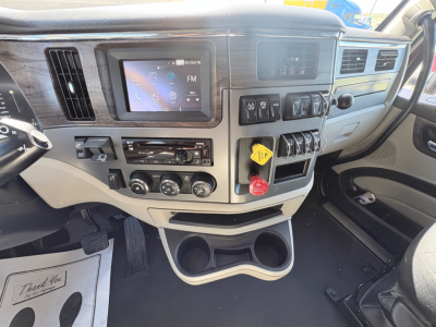 Peterbilt 579 truck interior dashboard view showing touchscreen infotainment, control switches, yellow locking tab and red push-to-release button, cup holders and storage below dash.