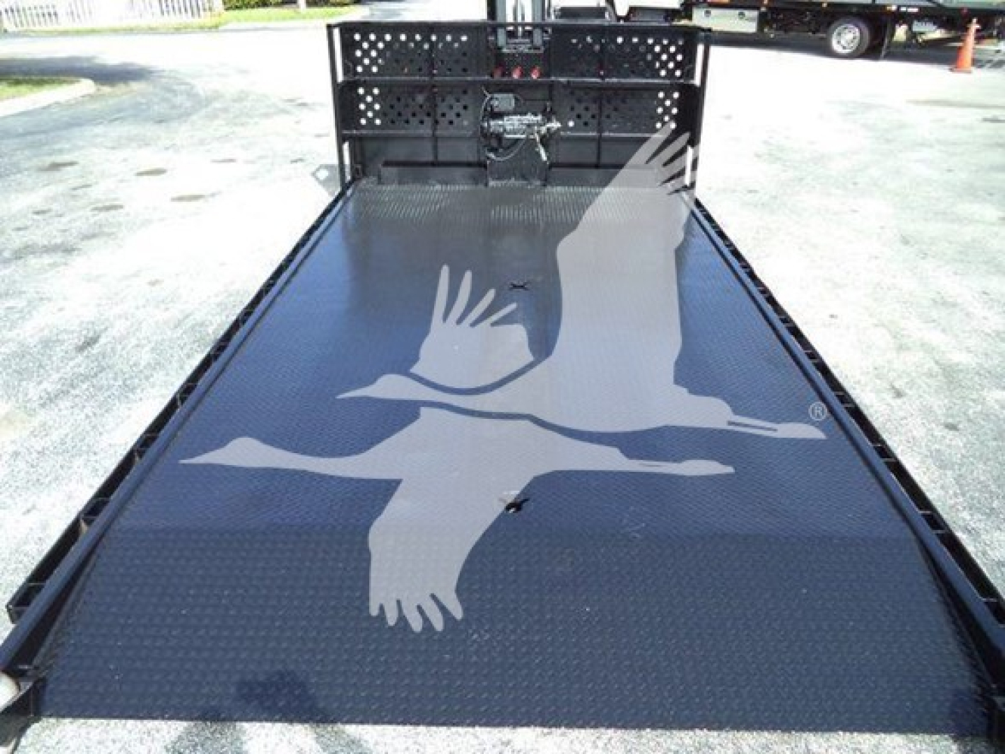 Flatbed truck bed with black diamond plate platform and rear hooklift ramp; Hino 258LP site image with cage and towing gear visible.
