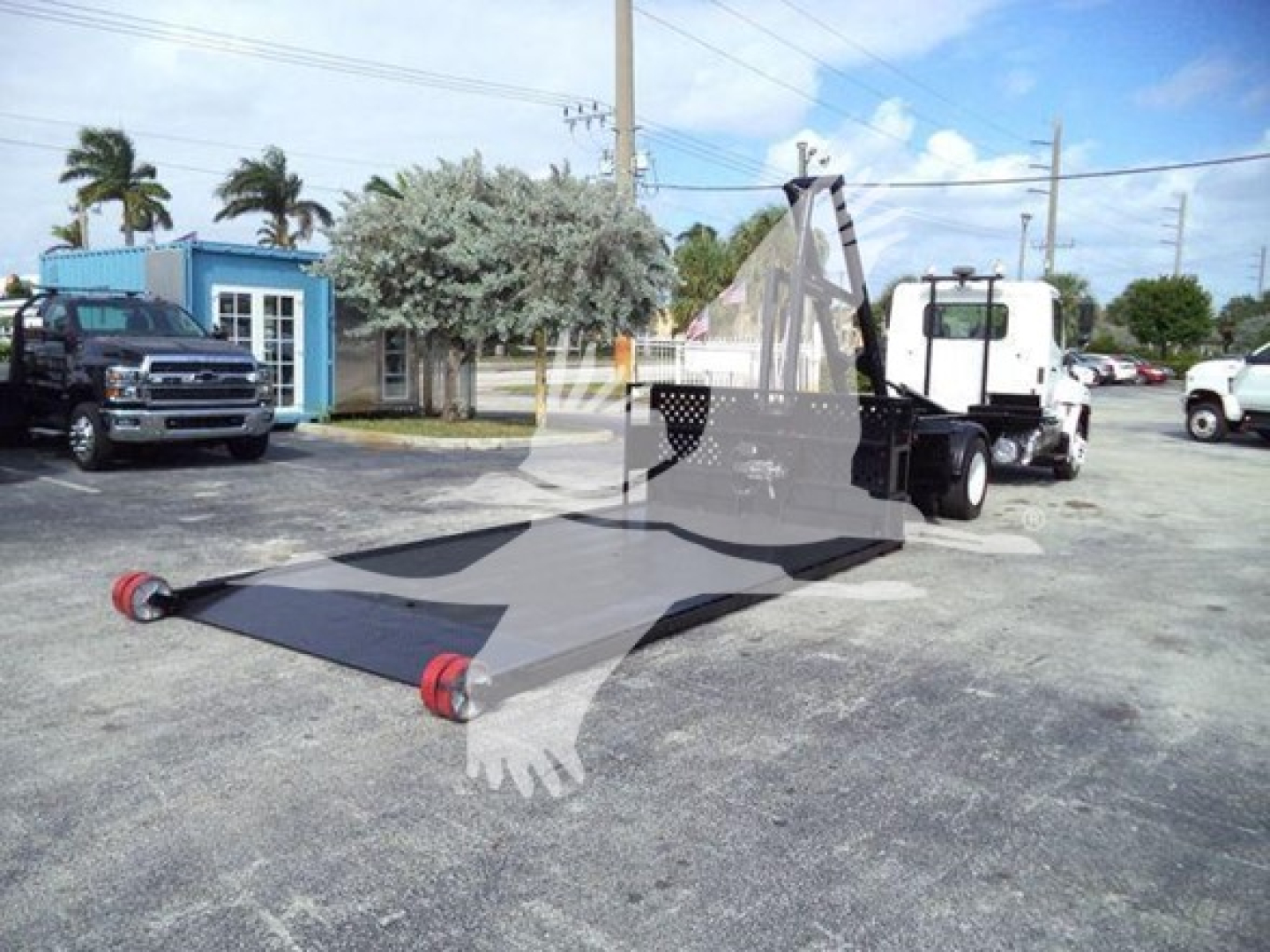 Image of a 2017 Hino 258LP hooklift truck with a deployed flatbed/hooklift material picker in a lot, showing the chassis and cab in background.