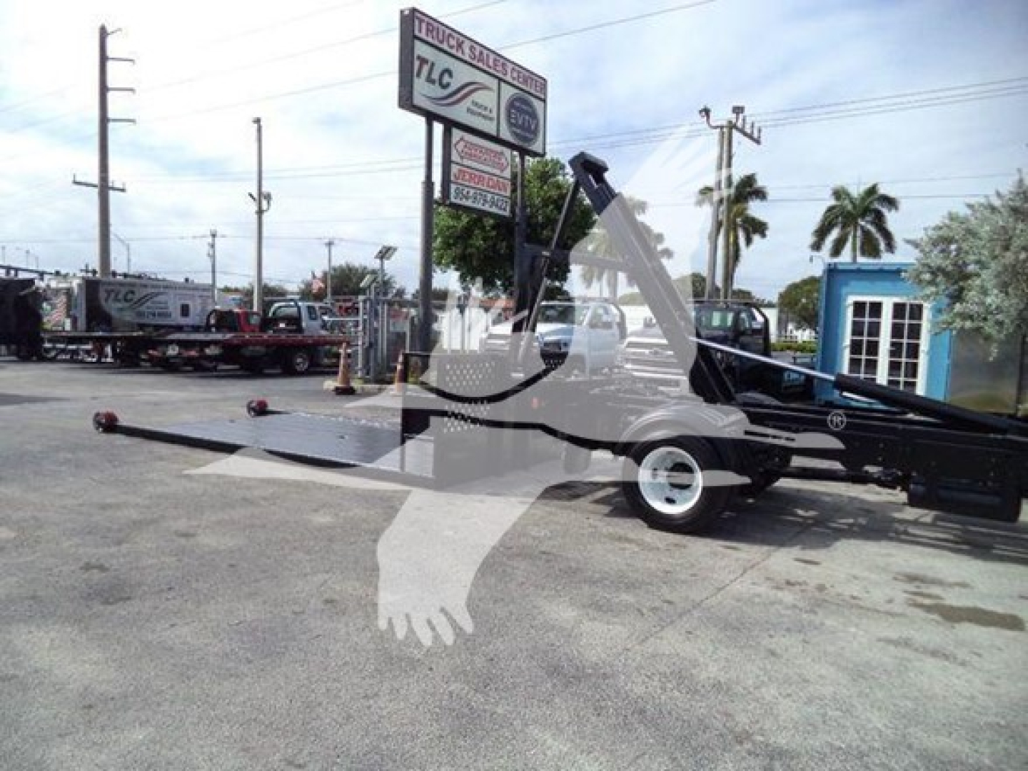 Truck yard scene showing a 2017 Hino 258LP hooklift truck with extended boom and trailer hitch in a used vehicle lot.