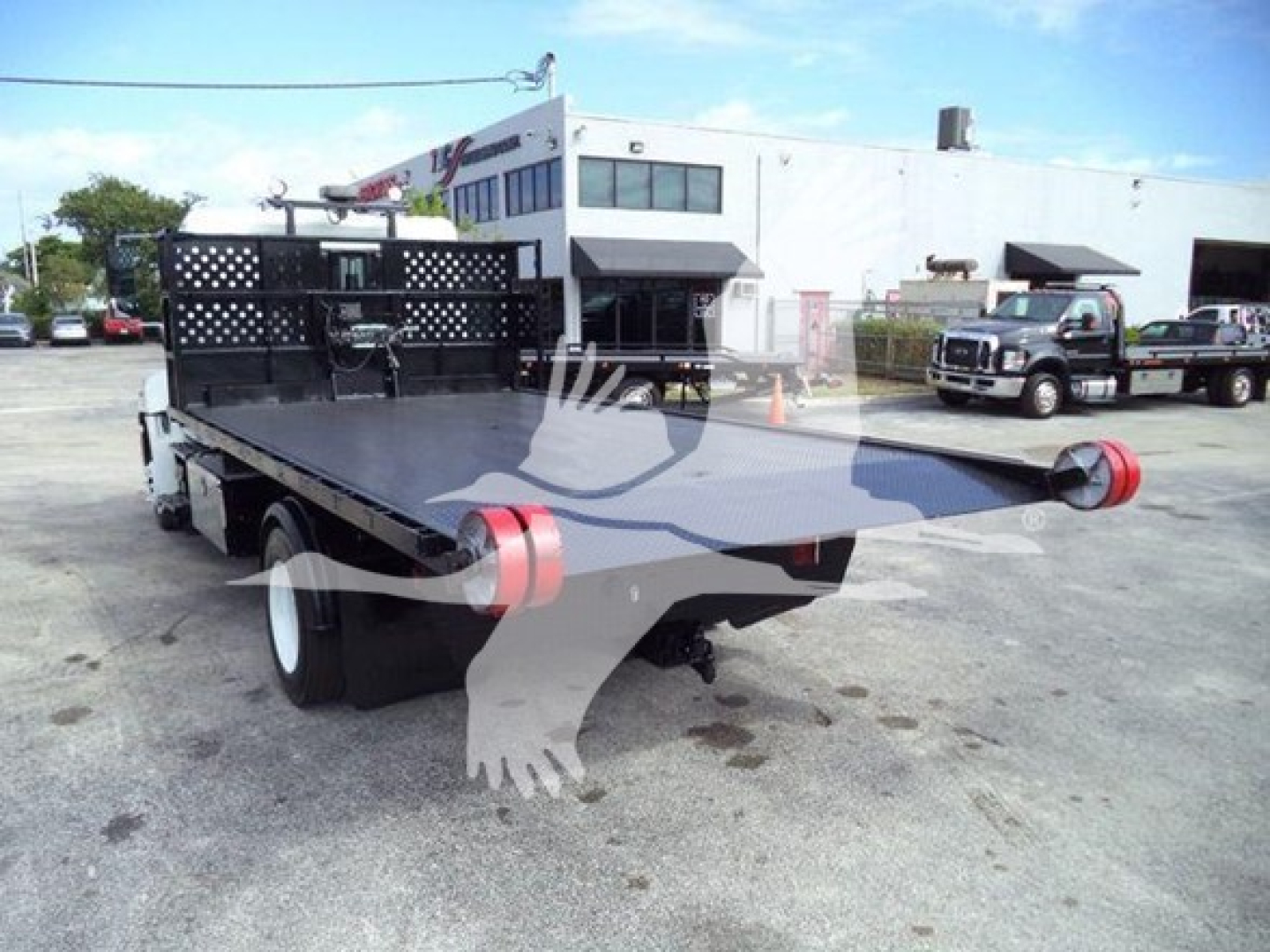 Hino 258LP hooklift truck bed with flatbed and rear tail lights, viewed from rear-right in a dealership lot.