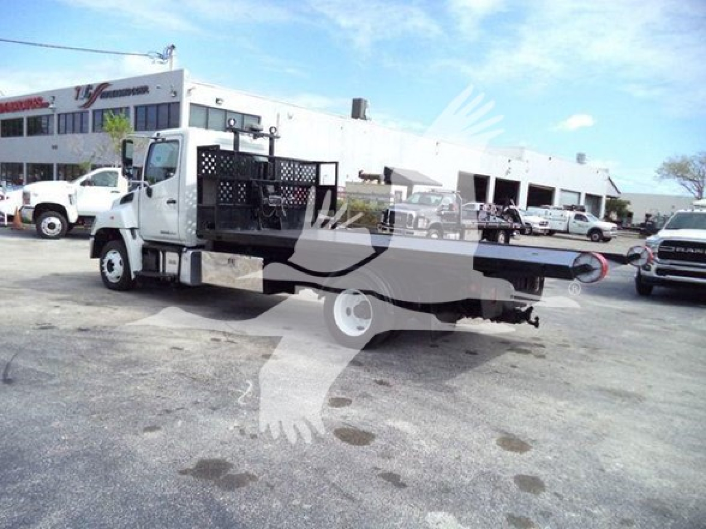 Hino 258LP hooklift truck side view showing flatbed rear and cab, with dealership lot in background.