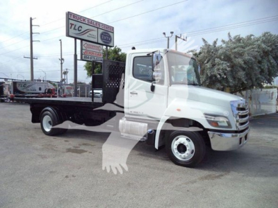 2017 Hino 258LP hooklift truck in a dealership lot showing cab and flatbed with sign in background.