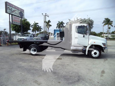 2017 Hino 258LP hooklift truck in a dealership lot with palm trees in background. Side view shows flatbed chassis and cab; TLC Truck Sales sign in distance.