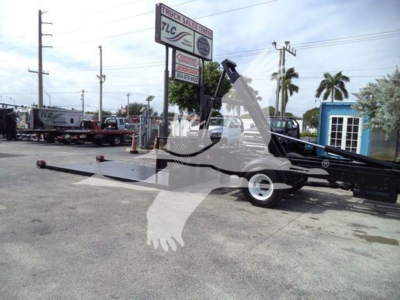 Truck yard scene showing a 2017 Hino 258LP hooklift truck with extended boom and trailer hitch in a used vehicle lot.