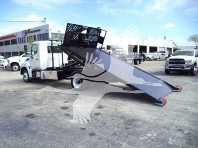Hino 258LP hooklift truck with tilted flatbed and raised loading platform in a dealership lot.