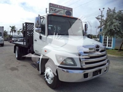 Hino 258LP hooklift truck front-left view with flatbed and chrome grille, white cab, side mirrors, and DOT bumper.