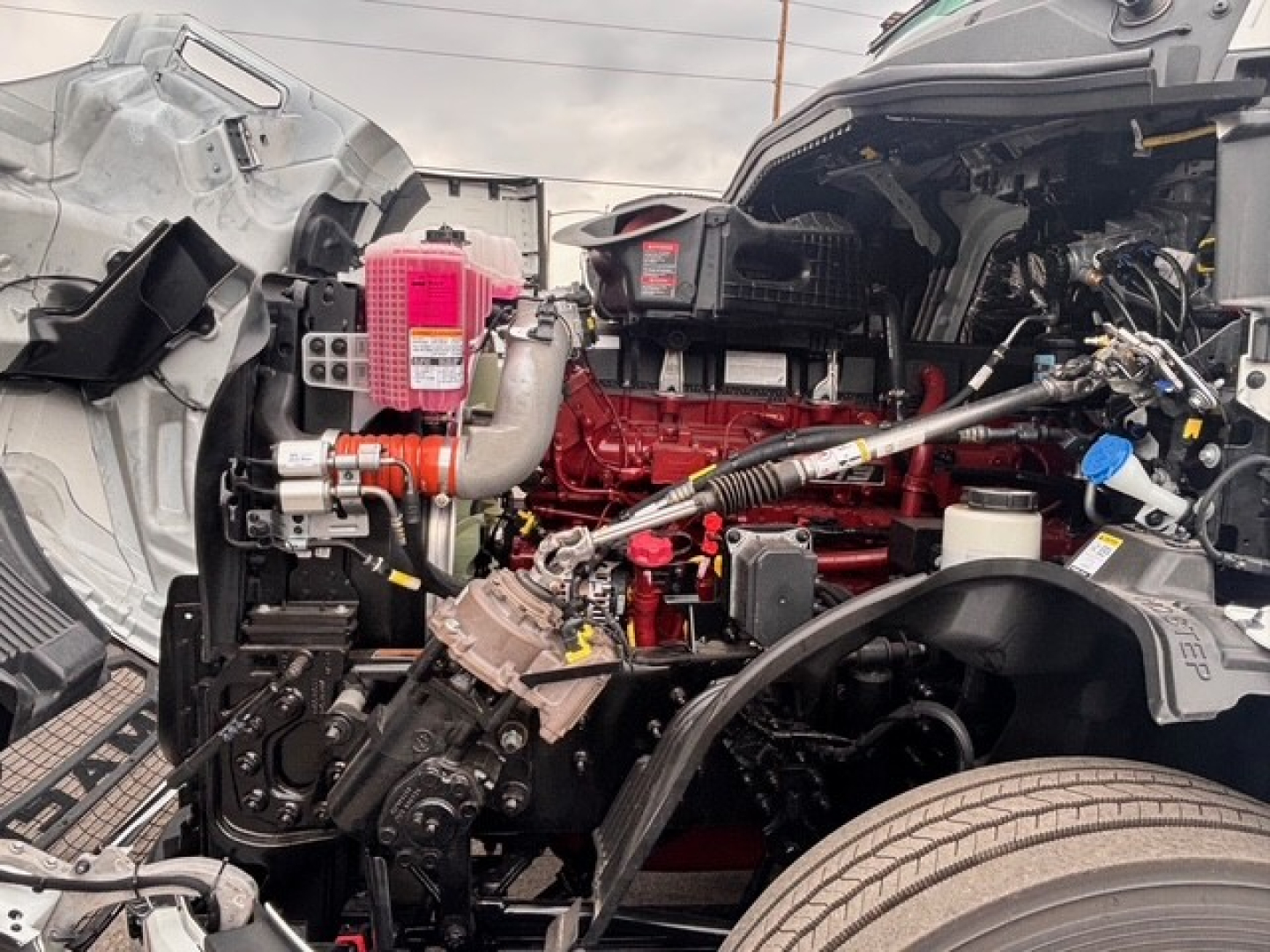 Truck engine bay with red engine block, pink coolant reservoir, hoses, and exposed components visible in a collapsed hood area.