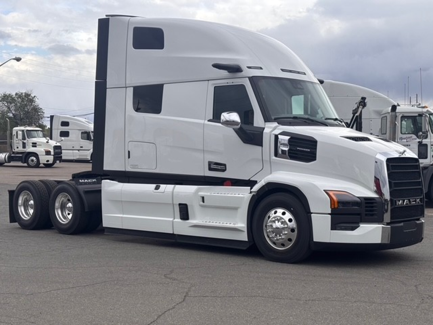 Truck side view showing 2026 Mack PR64T76H conventional sleeper tractor with white cab, dual rear axles, chrome mirrors, and black grille.