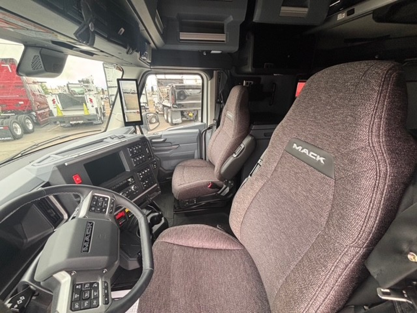 Cab interior of a new 2026 Mack PR64T76H tractor-trailer showing steering wheel, dashboard, and brown fabric seats with Mack branding.