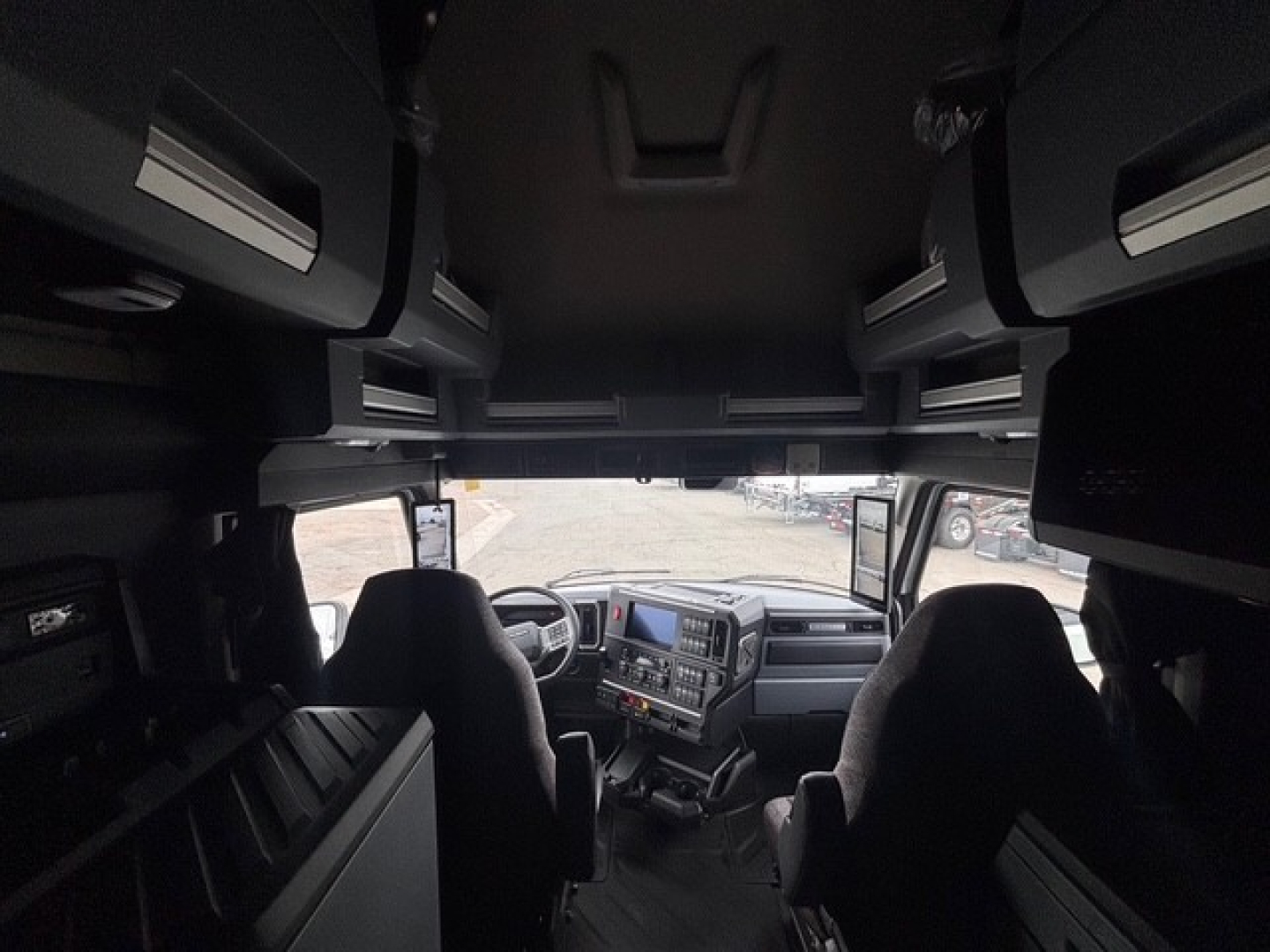 Truck cab interior of Mack PR64T76H showing driver and passenger seats, dashboard, overhead storage compartments, and side windows.