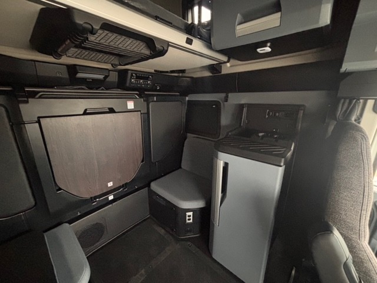 Cab interior of a new 2026 Mack PR64T76H sleeper tractor showing compact galley with fridge, storage, and cabinetry.