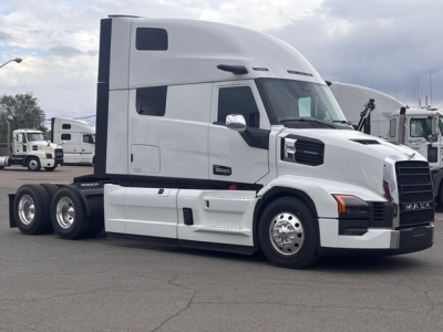 Truck side view showing 2026 Mack PR64T76H conventional sleeper tractor with white cab, dual rear axles, chrome mirrors, and black grille.