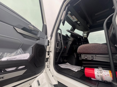 Truck cab interior with open door, dashboard and steering wheel visible; red fire extinguisher mounted near floor; seat and control panel visible.