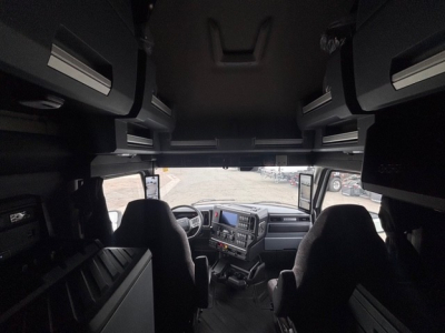 Truck cab interior of Mack PR64T76H showing driver and passenger seats, dashboard, overhead storage compartments, and side windows.