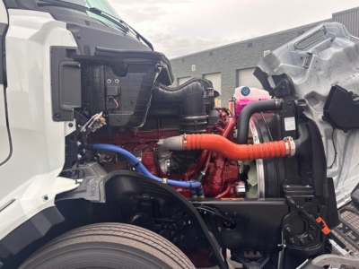Truck engine bay showing 6-cylinder engine with red block, blue and orange hoses, radiator and air intake components.