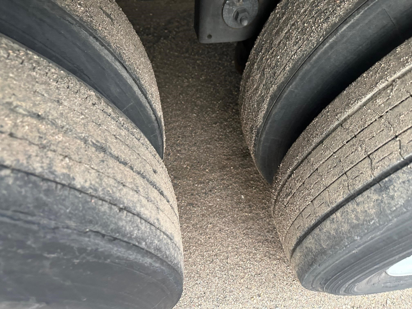 Close-up of dual rear tires on a trailer with gravel road debris between them.