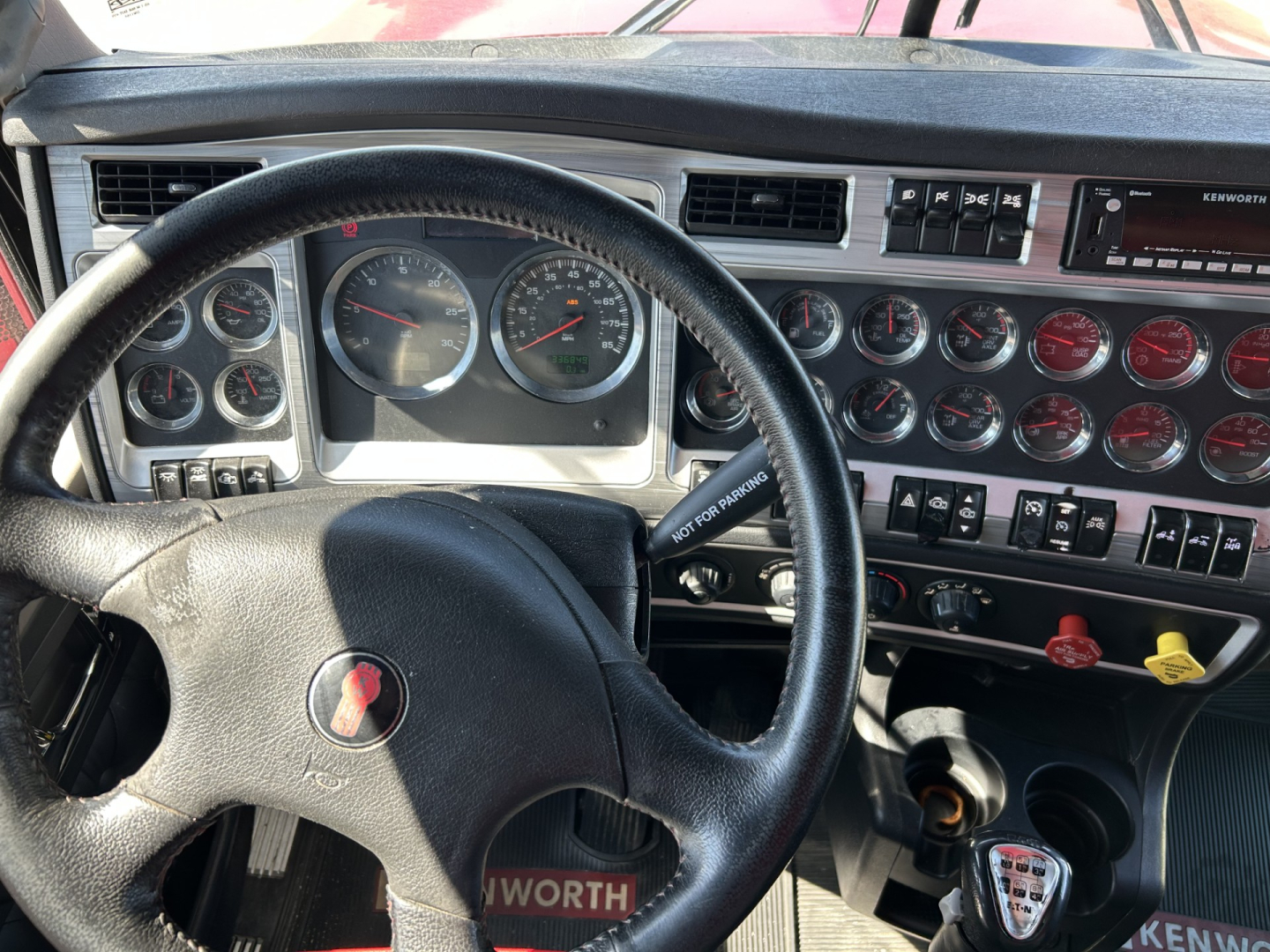 Kenworth W900L cab interior showing steering wheel and dashboard gauges with multiple round dials and switches.