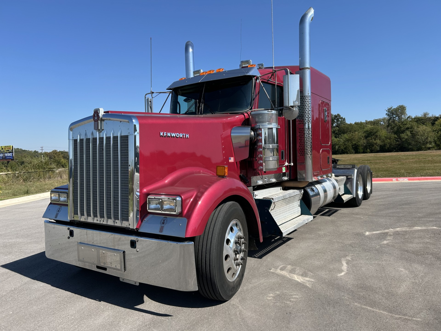 Kenworth W900L conventional sleeper truck in red with chrome grille, large exhaust stacks, and dual rear axles visible.