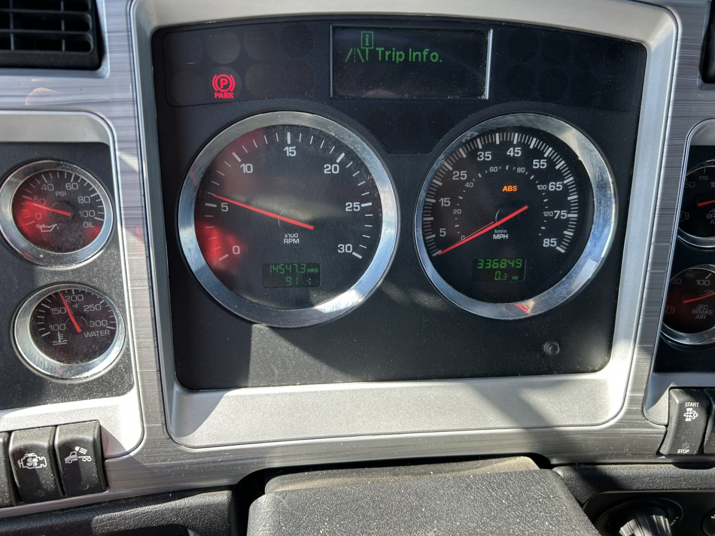Kenworth W900L dashboard showing dual round gauges and trip info display. Visible text includes 335,?? hours and ABS indicator, small digital readouts, chrome bezel gauges.