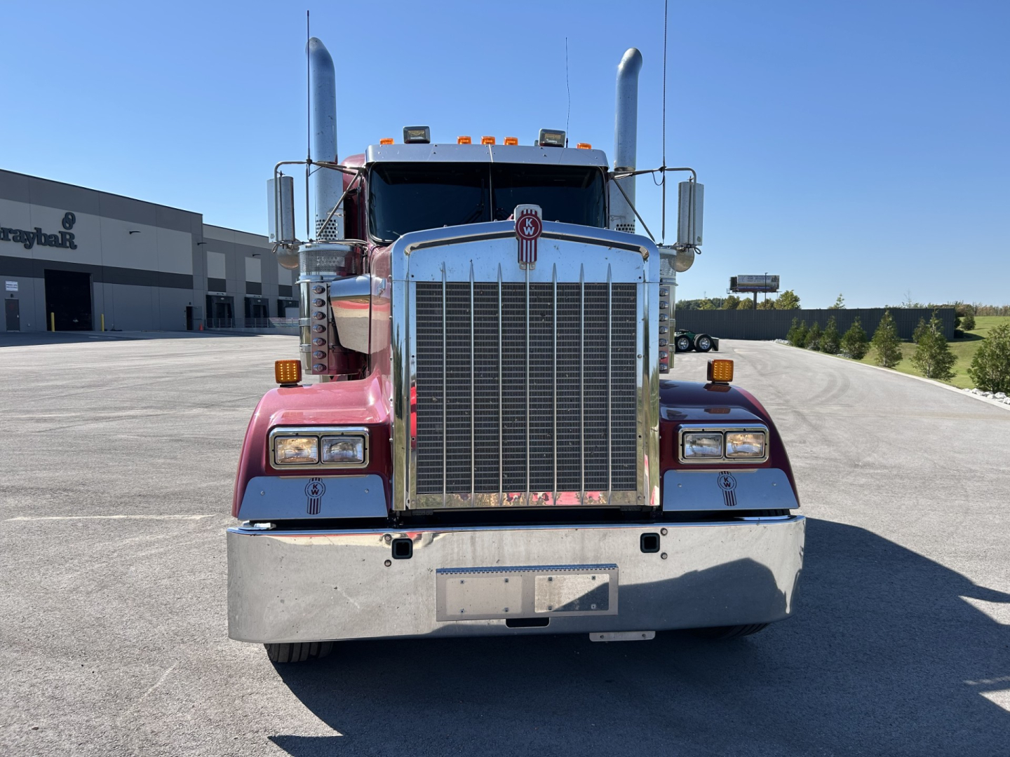 Kenworth W900L front view showing large chrome grille, dual vertical exhaust stacks, and bumper.