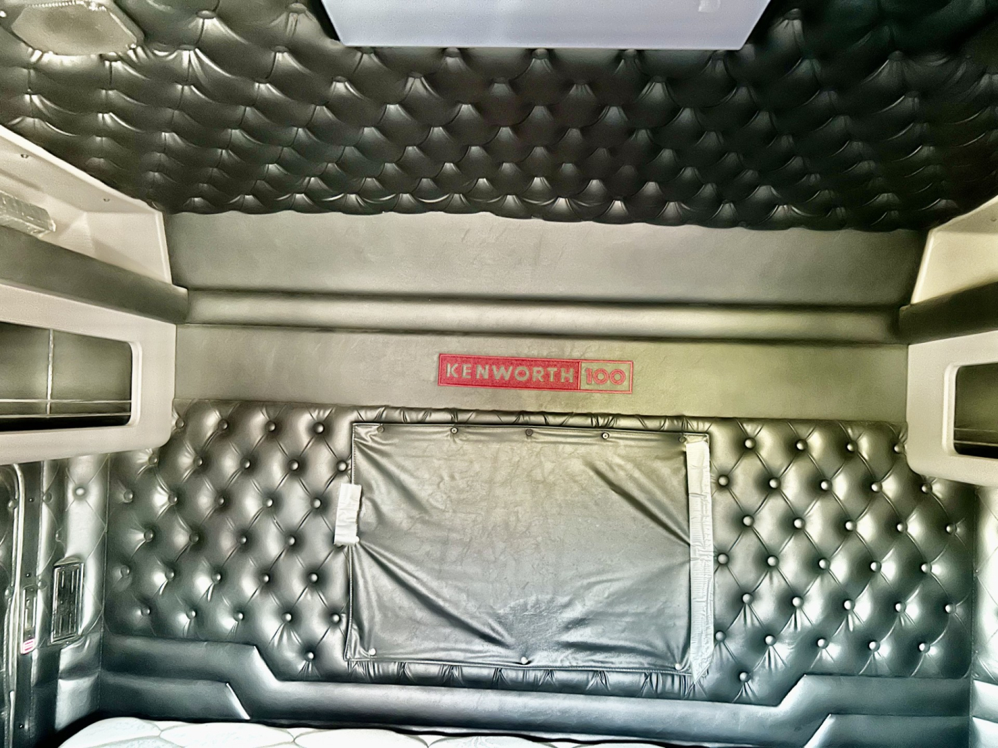 Kenworth W900L sleeper cab interior side panel with quilted black upholstery and Kenworth logo patch.