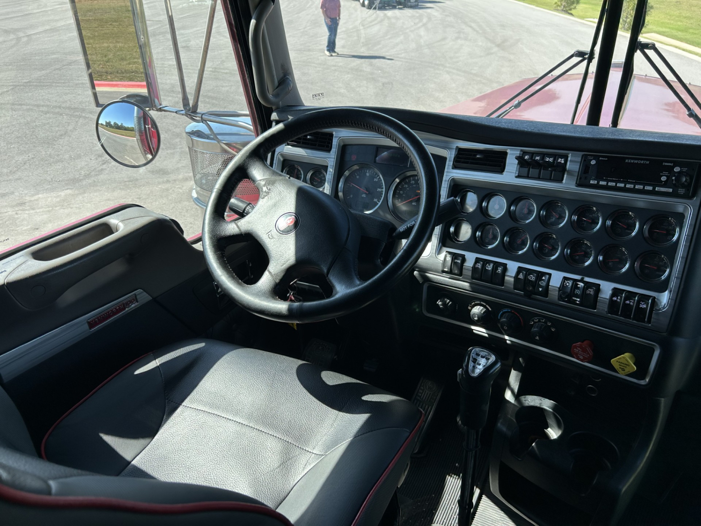 Interior of a Kenworth W900L truck cab showing steering wheel, instrument cluster, and dashboard controls in view.