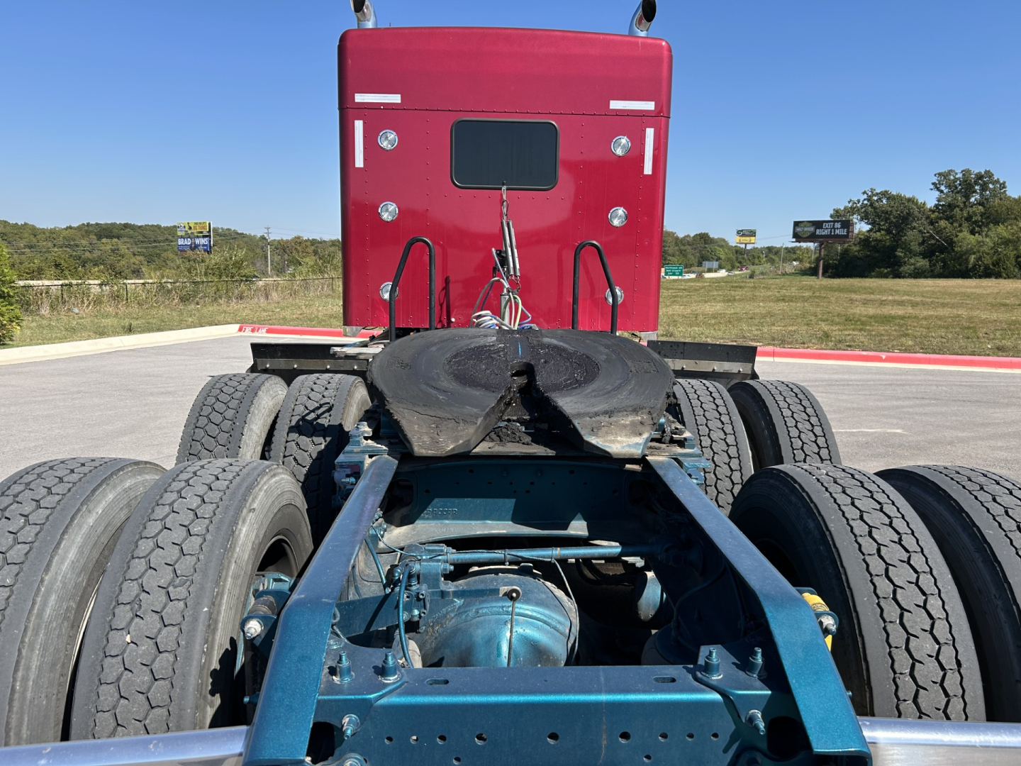 Kenworth W900L tractor rear view showing fifth wheel and dual rear axles with blue chassis and sleeper cab in background.