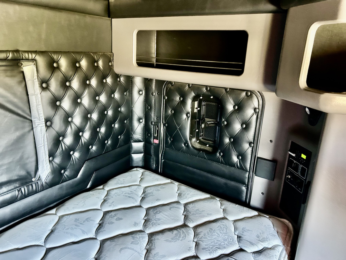 Kenworth W900L sleeper cab interior with quilted black leather upholstery and bed area.