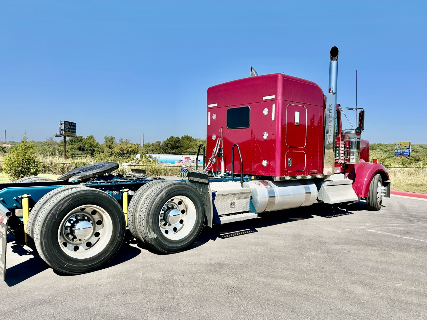 Kenworth W900L sleeper tractor cab rear/side view showing maroon cabin, dual rear axles, fuel tanks, and exhaust pipe.