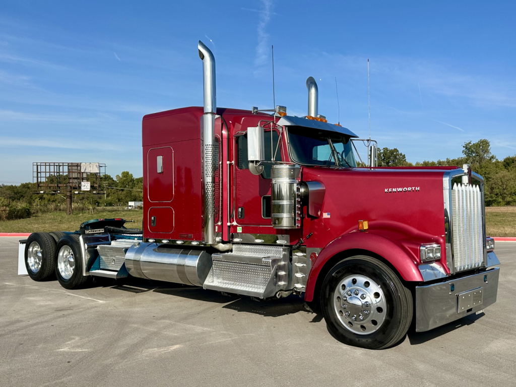 Kenworth W900L sleeper tractor in maroon with chrome exhaust stacks, side fuel tanks, and a long hood, side view showing front grille and wheels.