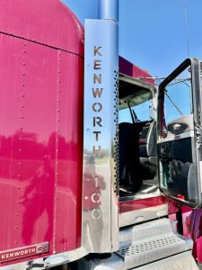 Kenworth W900L truck door area with chrome exhaust stack and pink cab;KENWORTH lettering on vertical chrome step; open driver door