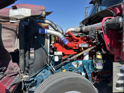 Kenworth W900L truck engine bay with red engine and blue coolant reservoir, wiring, and hoses visible.