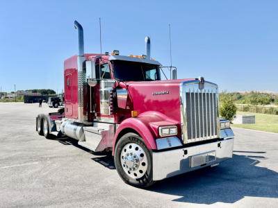 Kenworth W900L truck in red with chrome grille and tall exhaust stacks, front-left view showing large bumper, dual rear wheels, and sleeper cab.