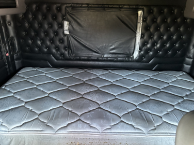 Kenworth W900L sleeper cab interior with quilted black leather bunk area and storage behind, showing a large bed in the back.