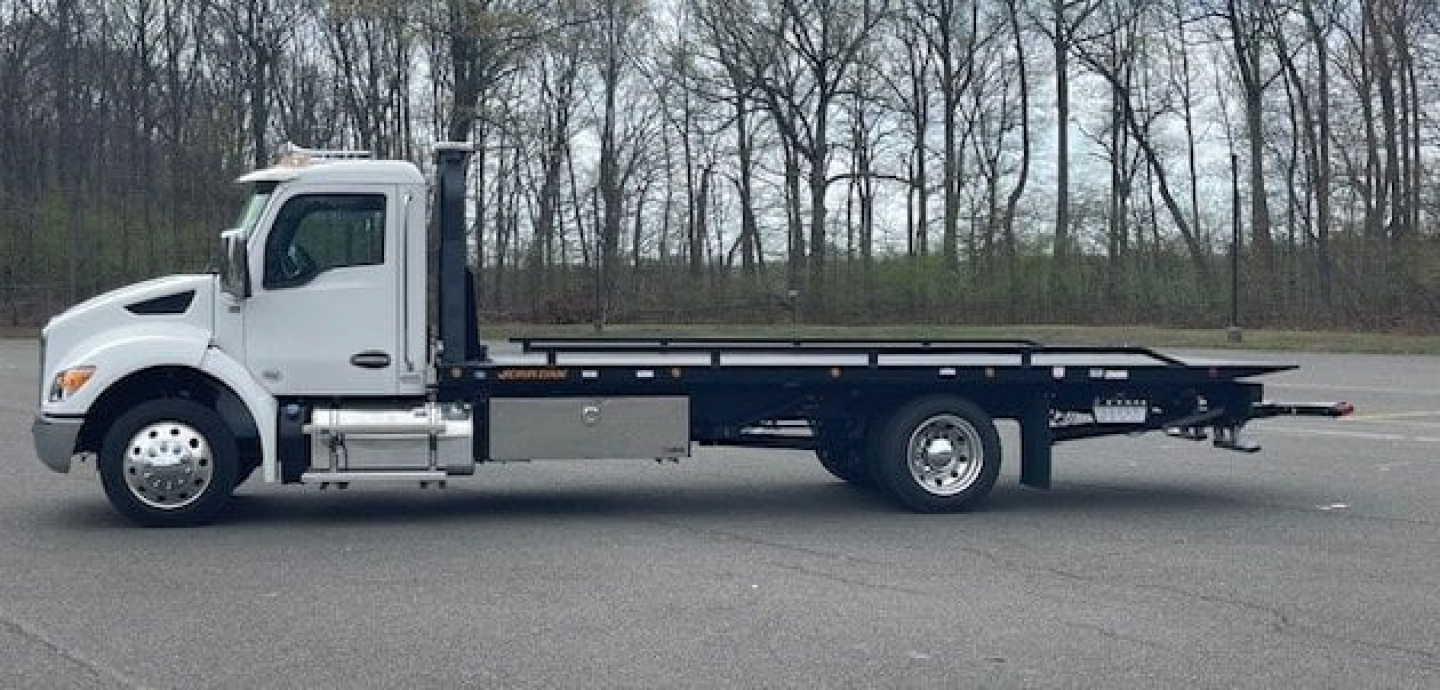 Kenworth T280 tow truck flatbed side view showing cab and long carrier bed with wheelbase, VIN and stock number not visible on image