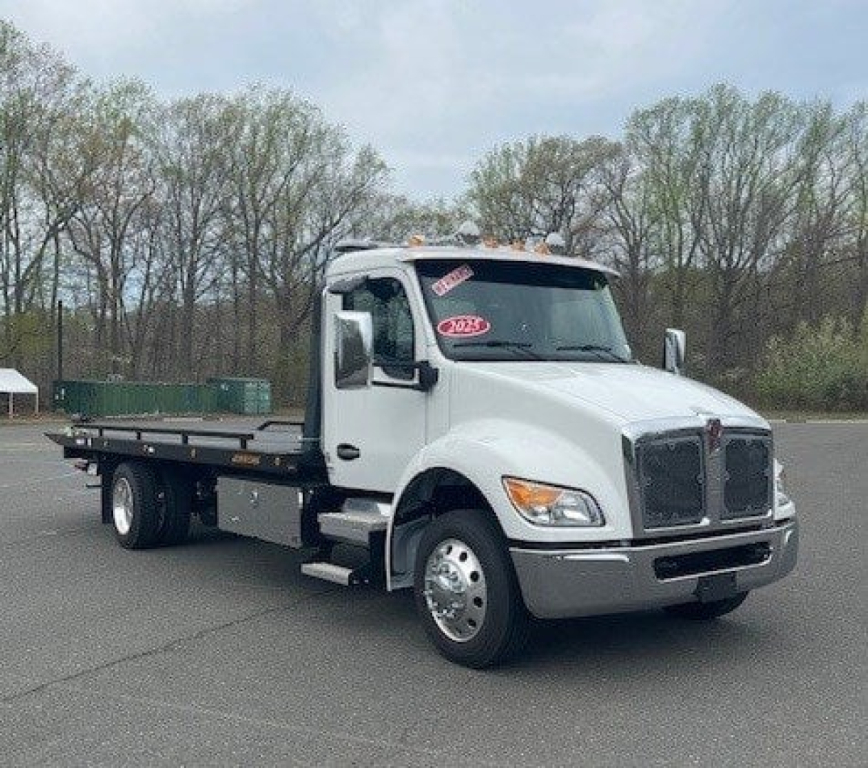 Kenworth T280 tow truck (flatbed) in silver/gray viewed from front-left, showing cab, flatbed, dual rear wheels, VIN tag not visible.