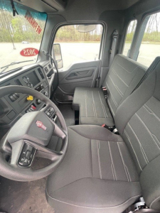 Truck cab interior showing steering wheel and front bench seat in a Kenworth T-line cab with dashboard controls.