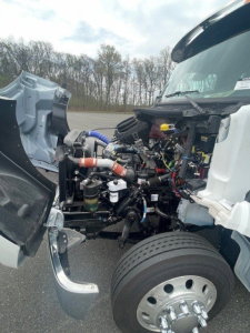 Kenworth truck engine bay with front fender removed showing engine components and hoses.