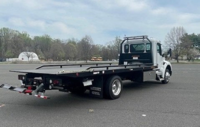 Kenworth T280 tow truck side rear view showing flatbed, rear lights, and tow hitch with reflective markers.
